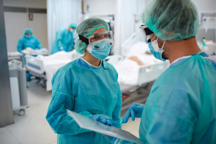 Healthcare professionals in protective gear talking in room with patients Healthcare professionals in protective gear talking in room with patients